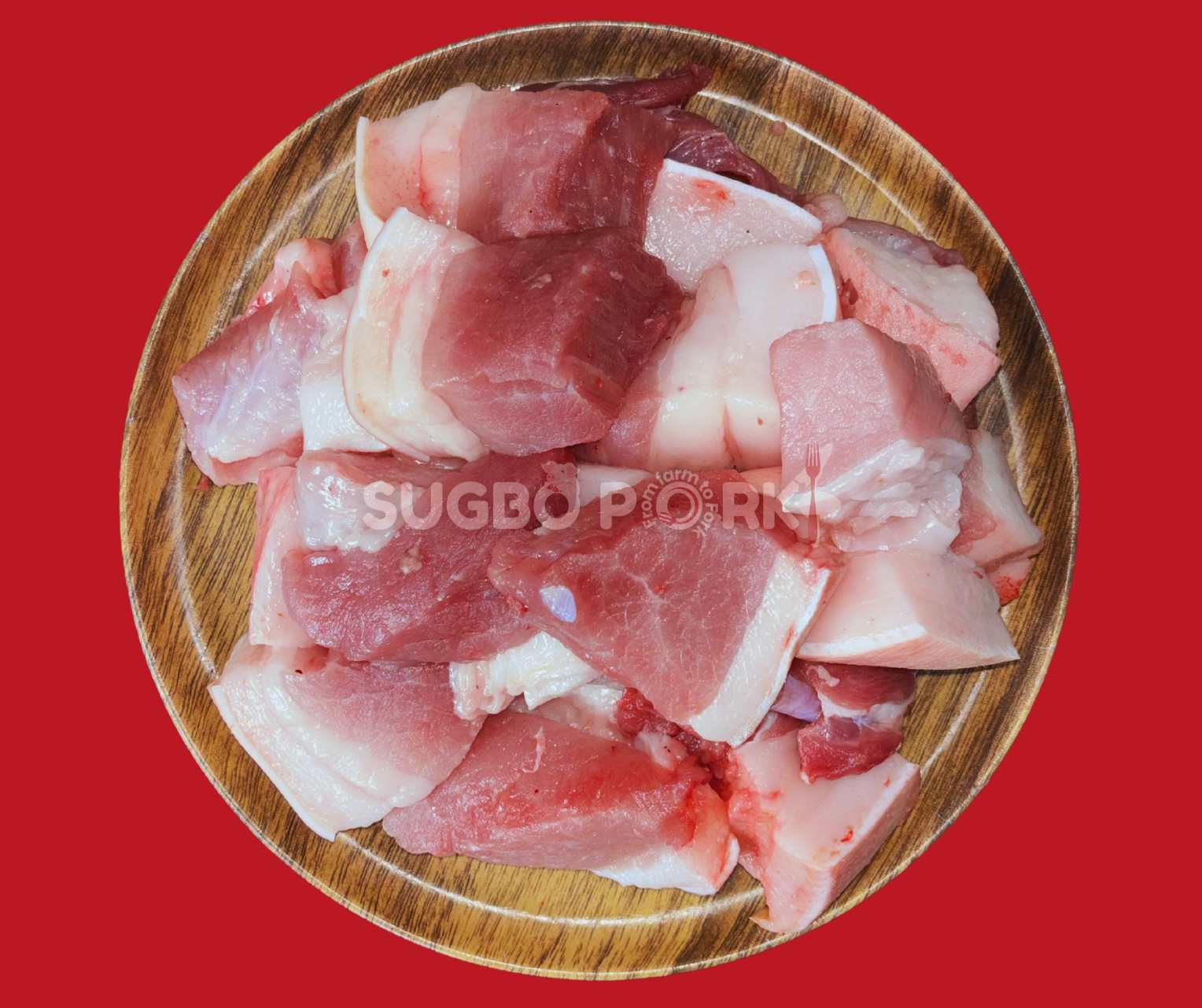 Professional product photography showing fresh humba cut pork pieces arranged on wooden circular cutting board with excellent marbling against vibrant red background with Sugbo Pork watermark