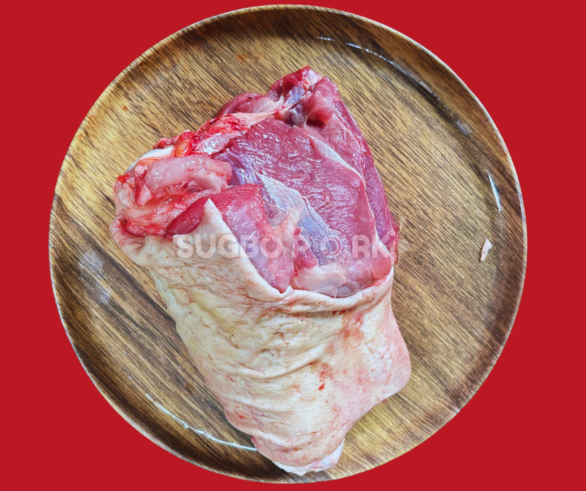 Professional product photography showing fresh pork leg pata on wooden circular board with excellent quality marbling against vibrant red background featuring Sugbo Pork watermark