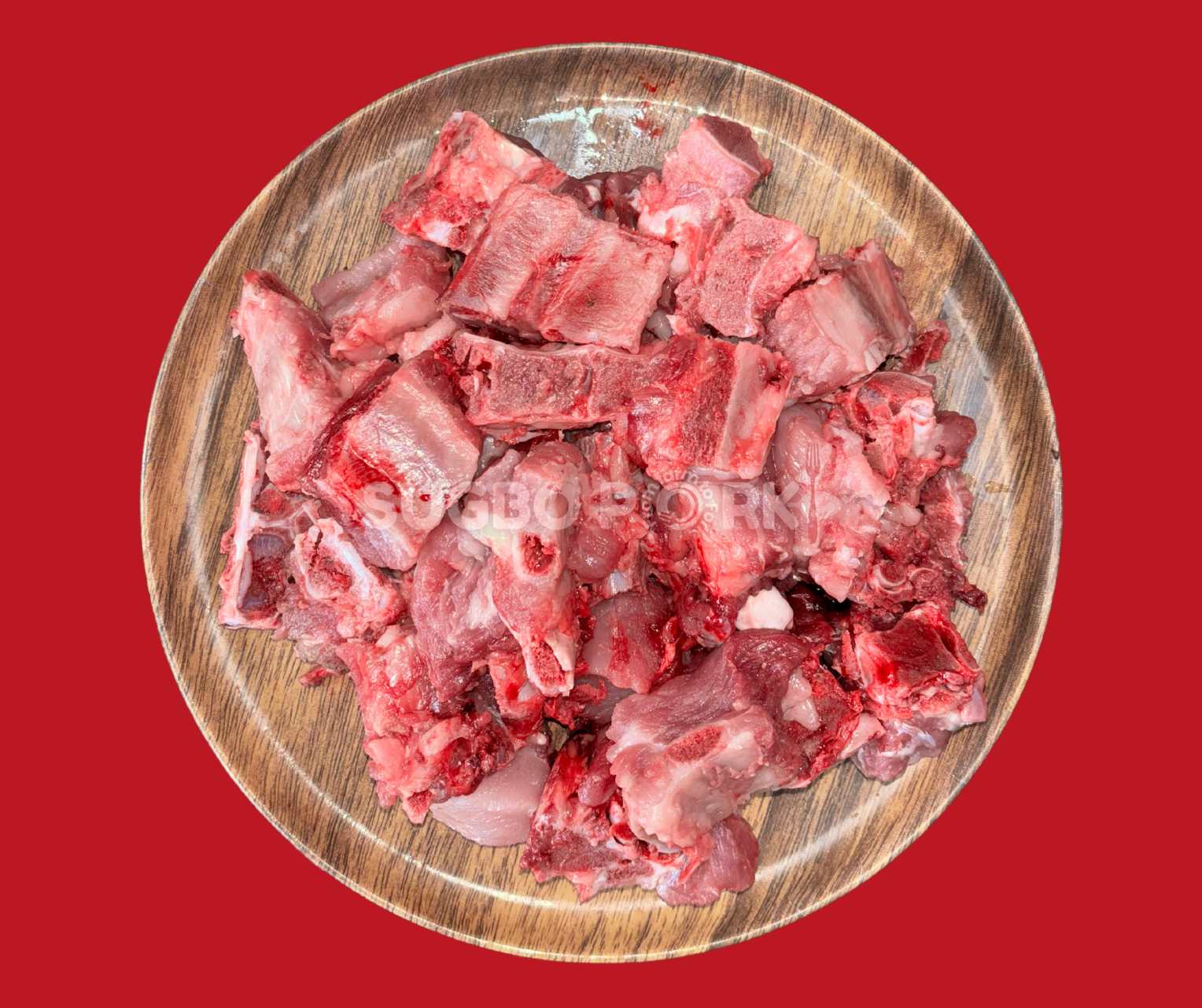 Professional product photography showing fresh pork riblets (small ribs) arranged on wooden circular plate with good marbling and natural coloring against vibrant red background, featuring Sugbo Pork watermark for brand consistency